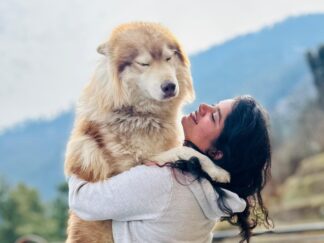 Solo woman traveler hugs a dog on a group trip in Kotgarh