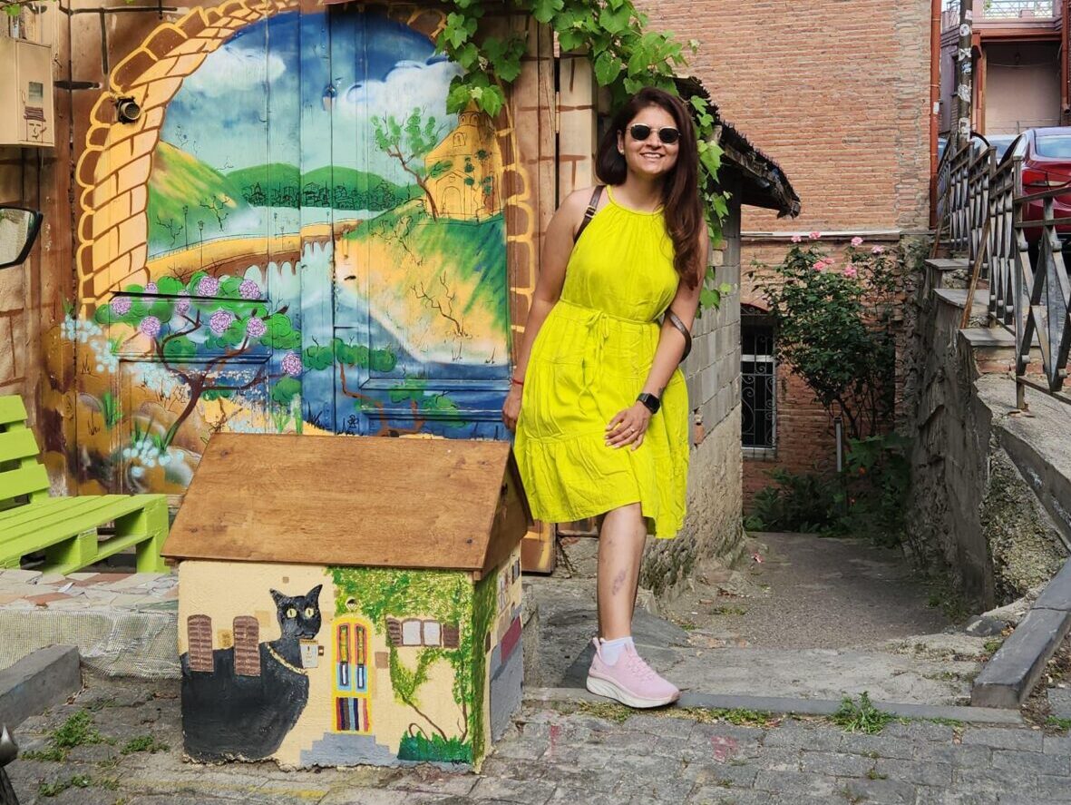 Female traveler in a bright yellow dress posing by vibrant street art in Old Tbilisi, Georgia