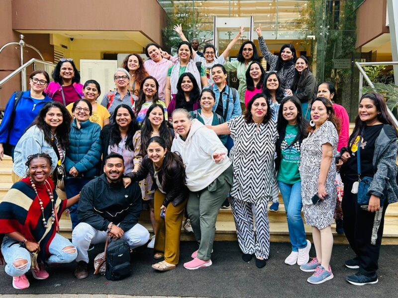 A joyful group of solo women travelers and their local hosts posing together outside a hotel during a Jugni Travel trip to Kenya, celebrating friendship, laughter, and new connections