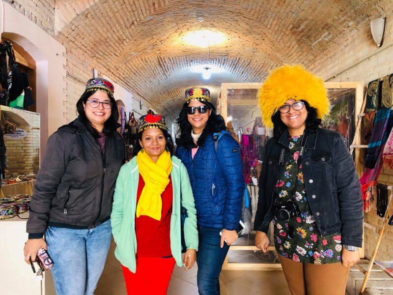 Four women travellers from India smiling and wearing colourful Turkish hats inside a local market during a Jugni Travel women-only trip to Turkey.