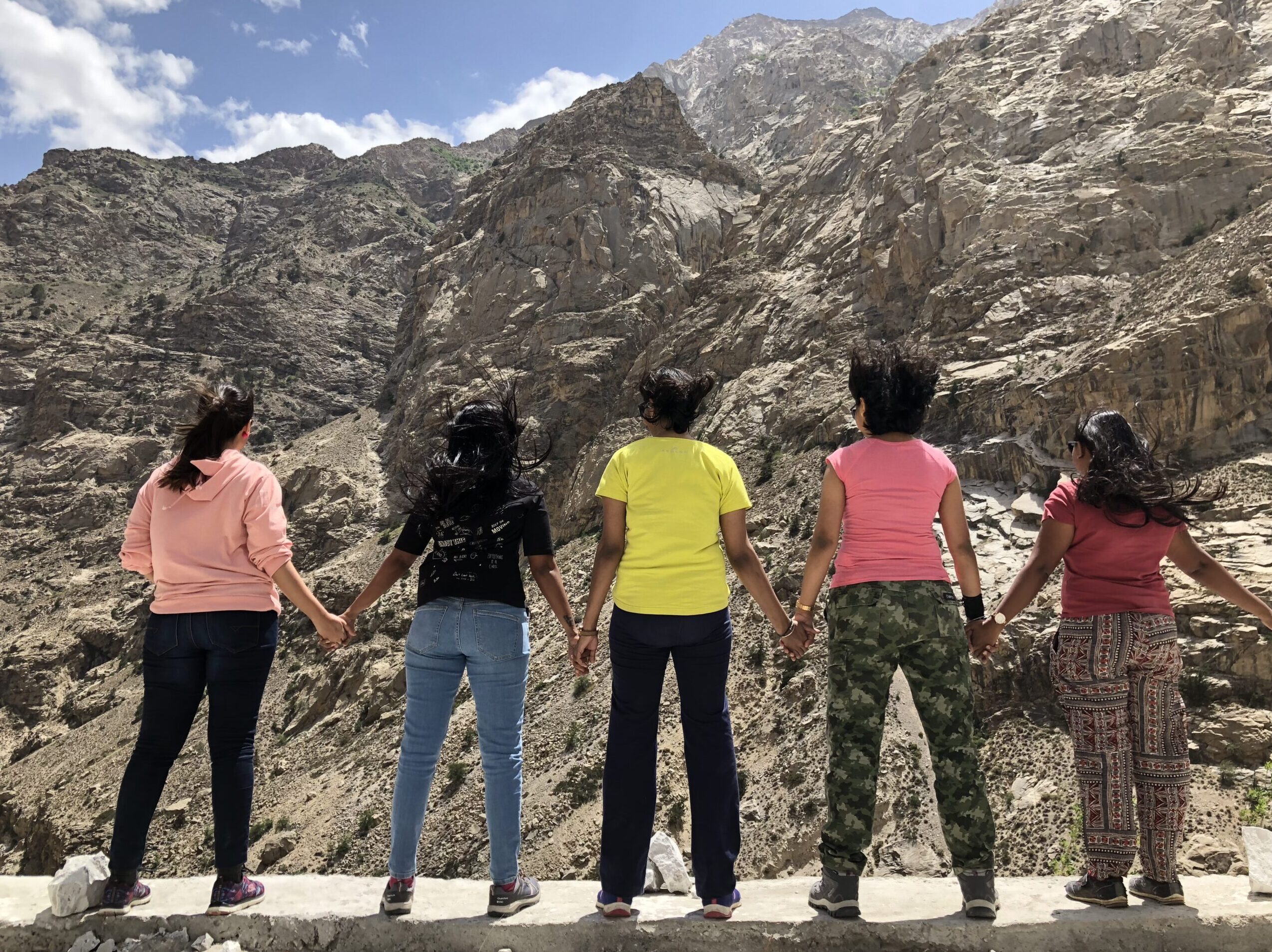 Five women travellers holding hands and standing strong against the cold Himalayan winds during a Jugni Travel road trip to Spiti Valley, India.