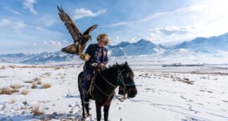Eagle hunter on horseback in snowy mountains of Kyrgyzstan – women-only cultural group travel experience.