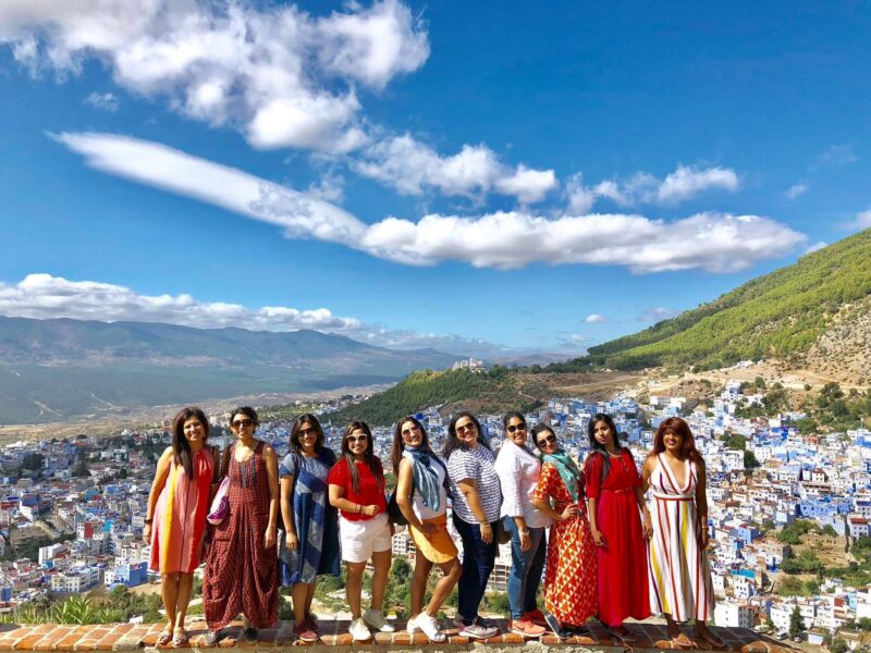 Women in their 50s and 60s on a Jugni women-only group trip in Morocco, posing joyfully above the blue town of Chefchaouen, celebrating that age is just a ticket number.
