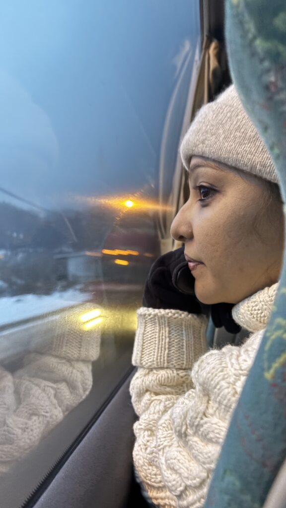 Solo woman traveler in winter sweater looking thoughtfully through a train window during a peaceful journey.