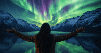 Woman experiencing her first solo trip in Norway under the Northern Lights, standing by a fjord with mountains and reflections
